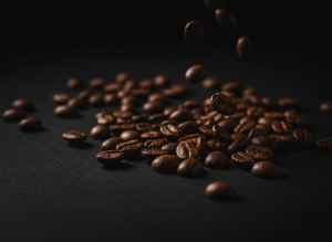 Ultra-dramatic cinematic close-up of dark roasted specialty coffee beans spilling across a matte black surface, moody chiaroscuro lighting with a single warm rim light, deep espresso browns fading to near-black shadows, editorial premium product photography, high contrast, shallow depth of field, no text