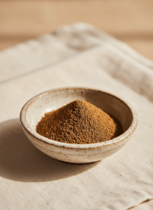 Close-up of roasted green tea hojicha powder in a small ceramic dish, warm toasty brown tones, soft natural light, cream linen background, editorial premium product photography, minimal