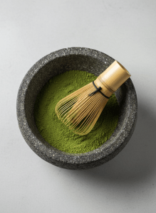 Overhead close-up of vibrant ceremonial matcha green powder in a stone bowl with a bamboo whisk, cream background, soft light, high-end editorial product photography, minimal negative space