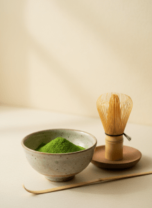 Elegant close-up of vibrant green ceremonial matcha powder in a small ceramic bowl next to a bamboo whisk, warm cream backdrop, soft diffused light, premium Japanese tea aesthetic, minimal styling, high-end product photography.