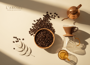 Premium editorial coffee brand hero image on a warm cream background. A beautifully composed flat-lay of freshly roasted whole coffee beans spilling from a matte ceramic vessel, alongside a single elegant pour-over setup, soft natural morning light, airy negative space, warm amber and toasted brown tones, high-end lifestyle photography, minimal and sophisticated.