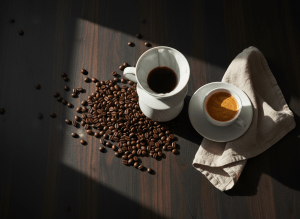 Premium editorial coffee flat lay. Wide landscape, top-down overhead shot on a rich dark espresso walnut wood surface. A white ceramic pour-over dripper mid-brew, freshly roasted whole coffee beans scattered naturally around it, a sleek white espresso cup with rich golden crema, a folded cream linen napkin beside it. Dramatic moody side lighting from the left, deep natural shadows. Deep espresso brown, black, warm amber, and cream tones. No text, no people, no logos, no watermarks. Shot like a Kinfolk or Monocle magazine spread. Cinematic depth of field.